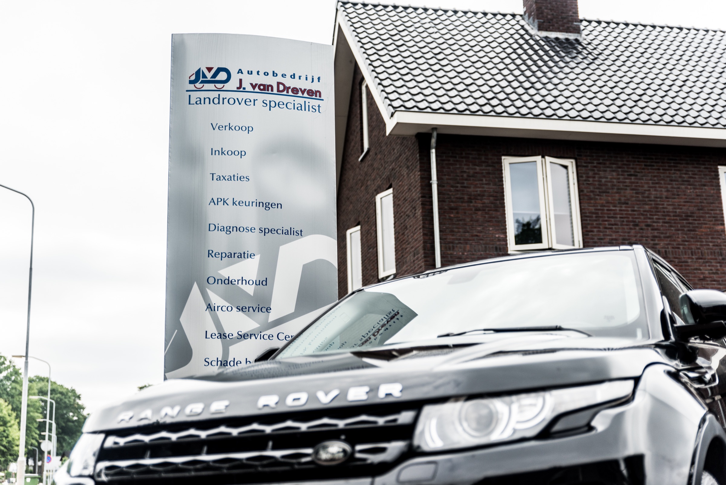 De reclamezuil van Autobedrijf J. van Dreven, Landrover specialist, met het woonhuis en een zwarte Range Rover Evoque op de voorgrond