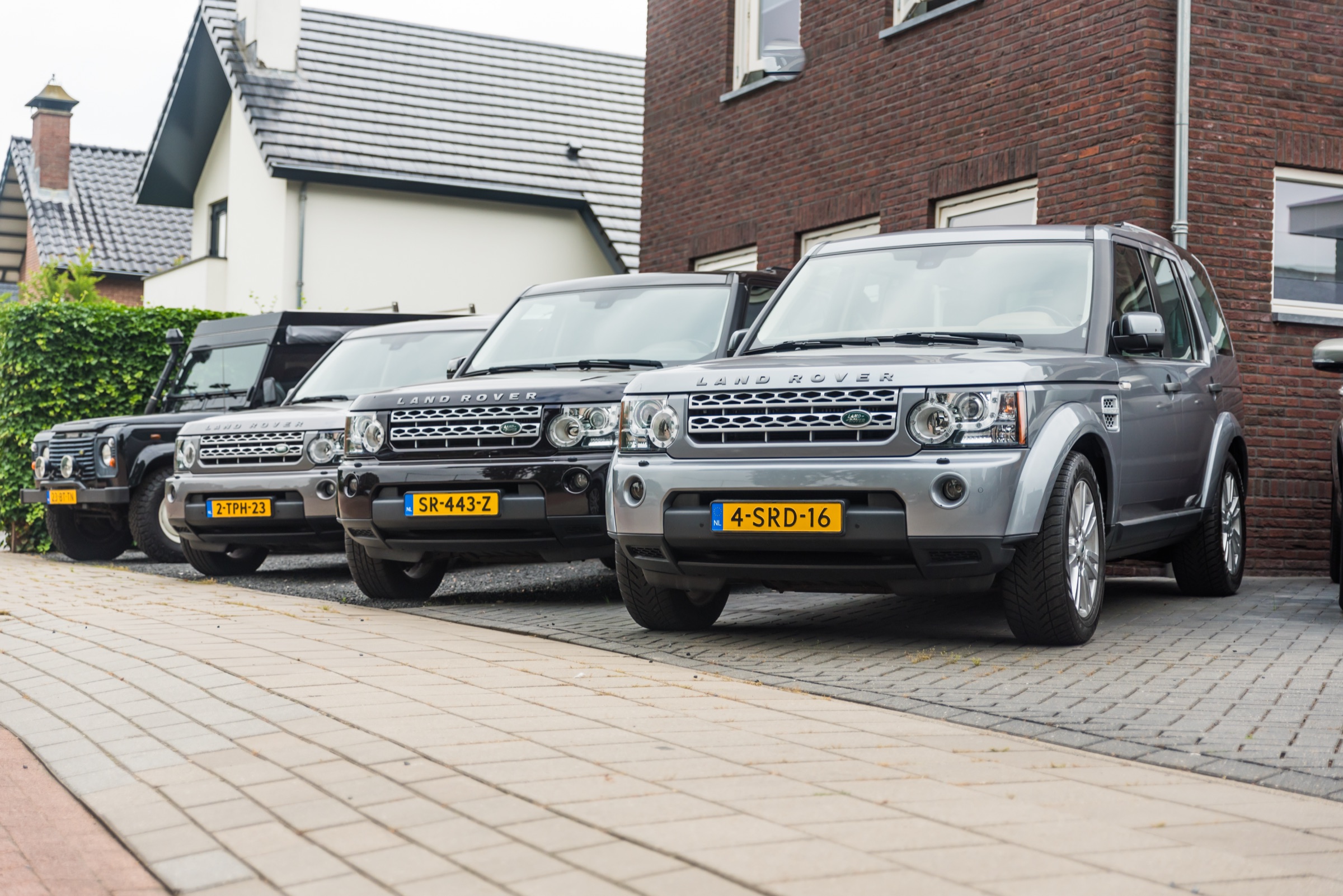 Een rij Land Rovers, Defender en Discovery 3 en 4, voor het bakstenen pand van Autobedrijf J. van Dreven