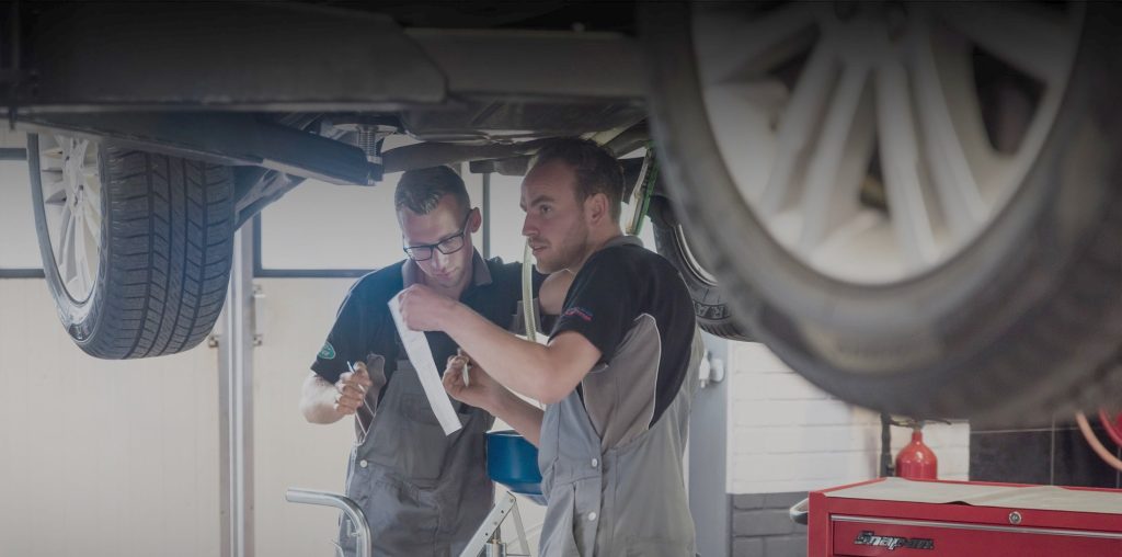 Twee monteurs bespreken de reparatie onder een auto op de brug